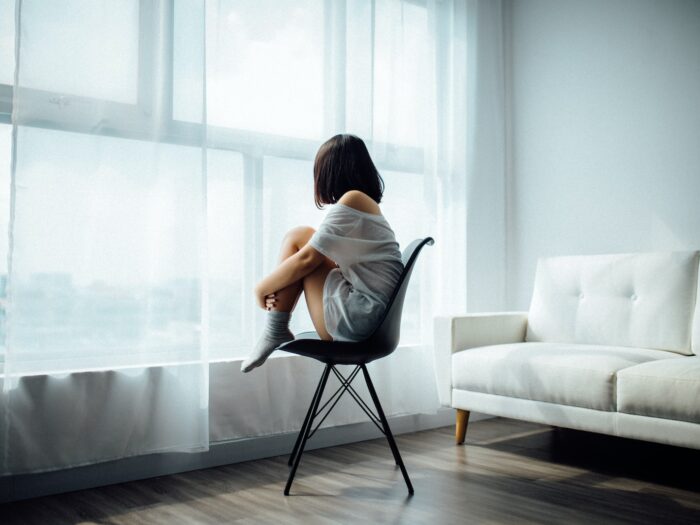 woman sitting on black chair in front of glass-panel window with white curtains